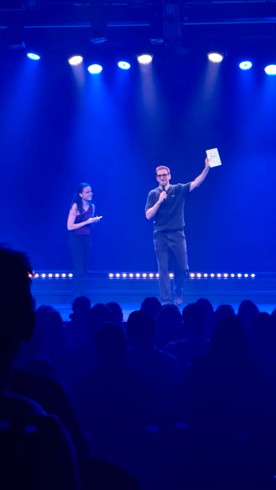 Léopold Lemarchand sur scène au Théâtre de l'Européen, tenant le portrait qu'Anne vient de dessiner de lui en direct